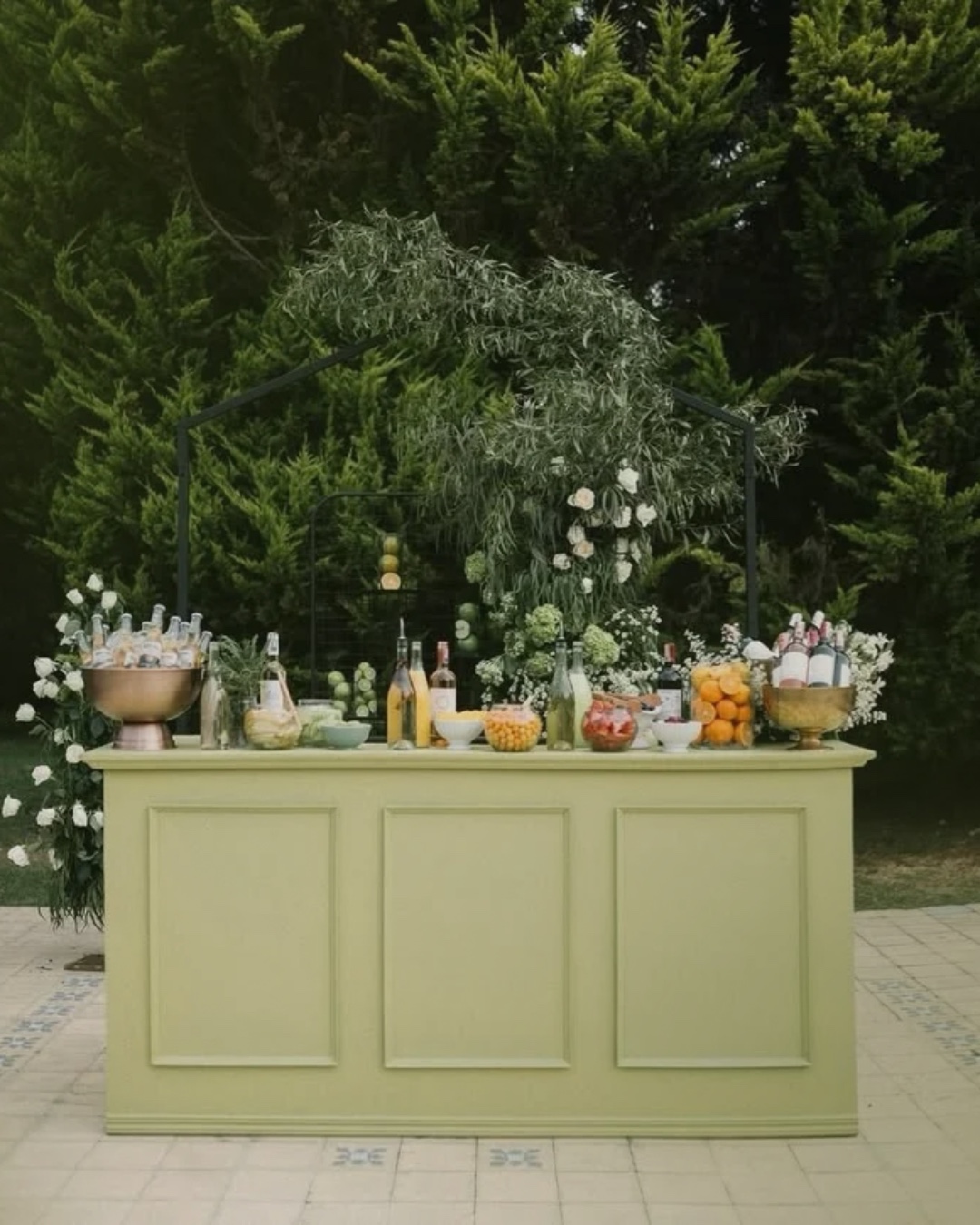 Bar mobile vert sauge avec boissons, agrumes et décoration florale pour une réception en extérieur